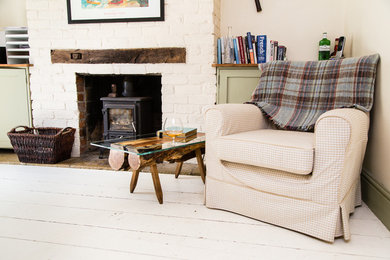 This is an example of a medium sized rustic open plan living room in Wiltshire with a reading nook, white walls, painted wood flooring, a wood burning stove, a brick fireplace surround and white floors.