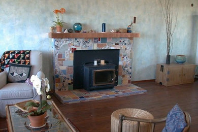Diseño de salón abierto de tamaño medio con paredes azules, suelo de madera oscura, estufa de leña y marco de chimenea de baldosas y/o azulejos
