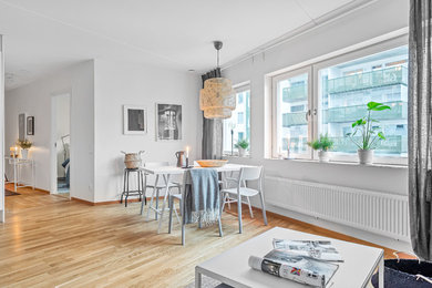 This is an example of a scandinavian open plan dining room in Stockholm with white walls, light hardwood flooring and beige floors.