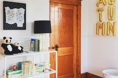 Ejemplo de habitación de bebé neutra moderna con paredes blancas y suelo de madera en tonos medios