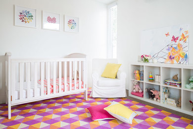 Modelo de habitación de bebé niña contemporánea de tamaño medio con paredes blancas, moqueta y suelo multicolor