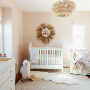 Diseño de habitación de bebé niña tradicional renovada con paredes rosas, suelo de madera oscura y suelo marrón