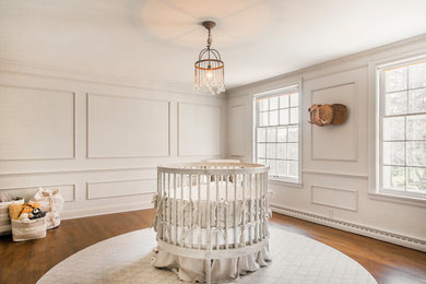 Modelo de habitación de bebé neutra tradicional renovada de tamaño medio con paredes beige y suelo de madera en tonos medios
