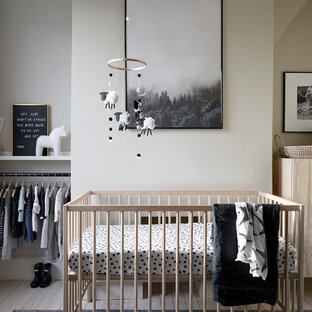Photo of a small scandinavian gender neutral nursery in London with white walls, light hardwood flooring and beige floors.