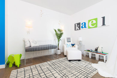 Cette photo montre une chambre de bébé garçon moderne de taille moyenne avec un mur blanc et un sol en bois brun.