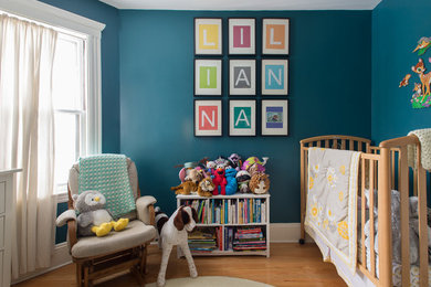 Modelo de habitación de bebé neutra clásica renovada con suelo de madera en tonos medios, paredes azules y suelo beige