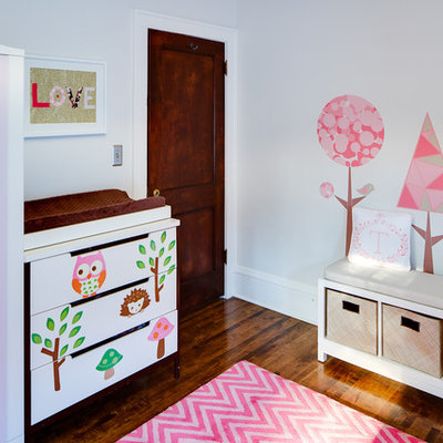 Trendy girl dark wood floor nursery photo in Minneapolis with white walls