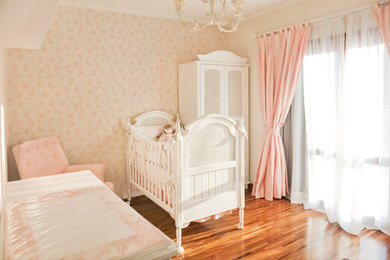 Ejemplo de habitación de bebé niña tradicional de tamaño medio con paredes rosas y suelo de madera en tonos medios