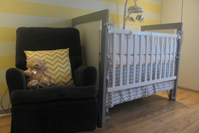 Diseño de habitación de bebé neutra clásica renovada pequeña con paredes amarillas, suelo de madera en tonos medios y suelo marrón