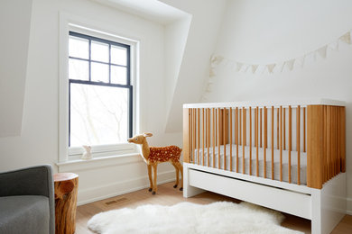 Ejemplo de habitación de bebé neutra actual con paredes blancas, suelo de madera en tonos medios y suelo marrón