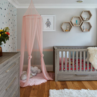 Inspiration for a large contemporary nursery for girls in Surrey with multi-coloured walls, medium hardwood flooring and brown floors.