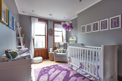 Photo of a medium sized bohemian nursery for girls in New York with grey walls and light hardwood flooring.