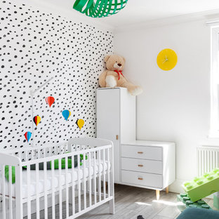 This is an example of a medium sized scandi gender neutral nursery in London with multi-coloured walls, light hardwood flooring, grey floors and wallpapered walls.
