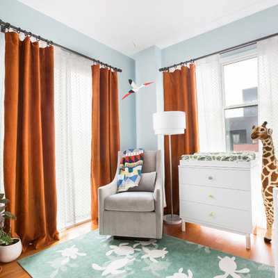 Trendy gender-neutral brown floor and medium tone wood floor nursery photo in New York with blue walls