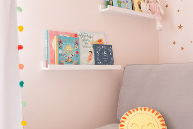 This is an example of a small eclectic nursery for girls in Los Angeles with pink walls, light hardwood flooring and yellow floors.