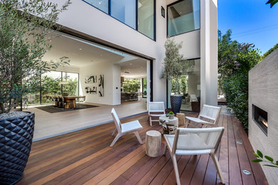 Example of a huge minimalist side yard patio design in Los Angeles with a fire pit, decking and a roof extension
