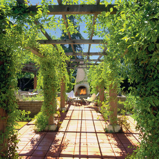 Immagine di un grande patio o portico american style dietro casa con un focolare, piastrelle e una pergola