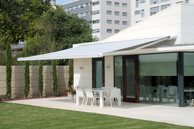Diseño de patio actual de tamaño medio en patio trasero con adoquines de hormigón y toldo