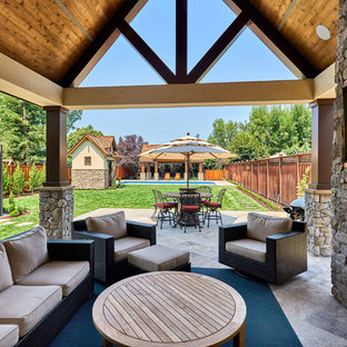 Foto di un ampio patio o portico country dietro casa con pavimentazioni in pietra naturale, un tetto a sbalzo e un caminetto
