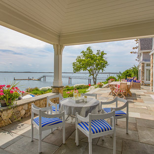 Immagine di un grande patio o portico costiero dietro casa con pavimentazioni in pietra naturale e un tetto a sbalzo
