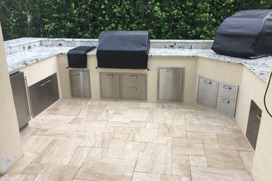 Example of an island style backyard stone patio kitchen design in Miami with no cover
