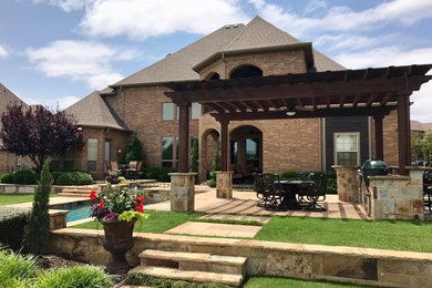 Design ideas for an expansive traditional back patio in Dallas with an outdoor kitchen, natural stone paving and a pergola.