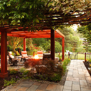 Foto di un patio o portico shabby-chic style dietro casa con un focolare, pavimentazioni in pietra naturale e una pergola