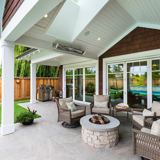 Immagine di un patio o portico stile marino di medie dimensioni e dietro casa con un focolare, piastrelle e un tetto a sbalzo