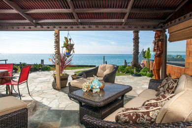Expansive coastal back patio in Orange County with natural stone paving, a roof extension and a water feature.