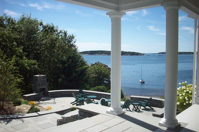 Large elegant side yard stone patio photo in Portland Maine with a fire pit