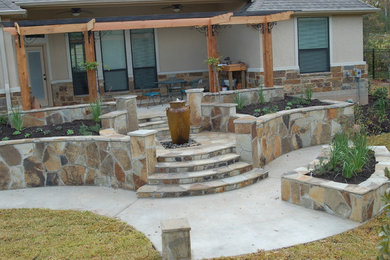 Example of a backyard concrete patio fountain design in Austin with a pergola