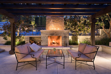 This is an example of a large modern back patio in Orange County with a fireplace, concrete paving and a pergola.