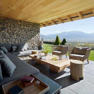Immagine di un patio o portico country dietro casa con pavimentazioni in pietra naturale e un tetto a sbalzo