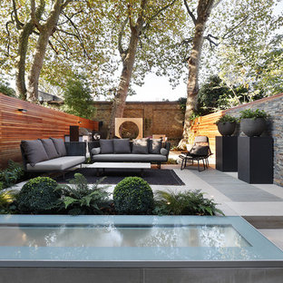 This is an example of a medium sized contemporary back patio in London with a potted garden and natural stone paving.