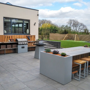 This is an example of a medium sized contemporary back patio in Hertfordshire with an outdoor kitchen, tiled flooring and no cover.