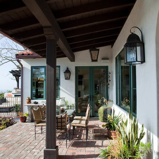 Immagine di un patio o portico mediterraneo di medie dimensioni e dietro casa con pavimentazioni in mattoni e un tetto a sbalzo