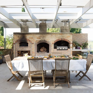 This is an example of a large country patio in Wollongong with an outdoor kitchen, concrete slab and a pergola.