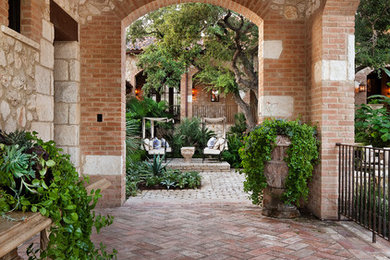 Example of a large tuscan side yard brick patio design in Austin with a roof extension