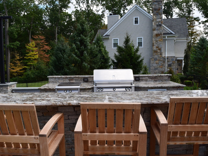 Example of a large, modern, stone patio fountain in the backyard with a pergola