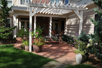 Mid-sized elegant backyard brick patio photo in Other with a pergola