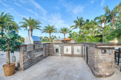 Patio kitchen - huge tropical backyard stone patio kitchen idea in Other with no cover