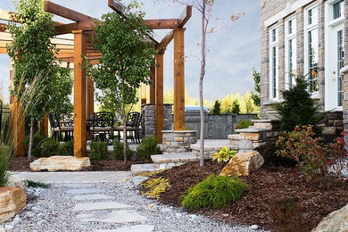 Large coastal back patio in Ottawa with natural stone paving, an outdoor kitchen and a pergola.
