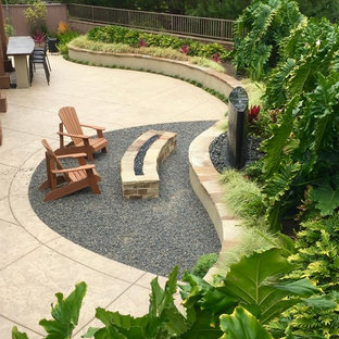 Foto di un patio o portico tropicale di medie dimensioni e dietro casa con un focolare, ghiaia e un tetto a sbalzo
