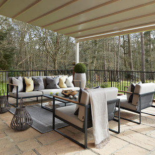 This is an example of a traditional back patio in London with natural stone paving and a roof extension.