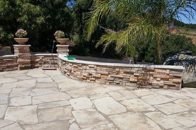 Cette photo montre une grande terrasse arrière tendance avec des pavés en pierre naturelle, aucune couverture et une cuisine d'été.