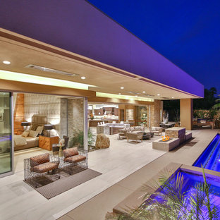 Foto di un ampio patio o portico design dietro casa con un focolare, piastrelle e un tetto a sbalzo