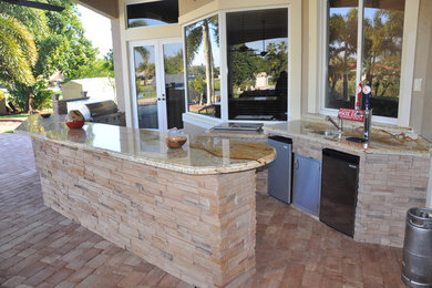 Patio kitchen - huge contemporary backyard stone patio kitchen idea in Miami with a roof extension