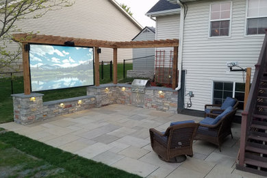 Example of a mid-sized classic backyard stone patio kitchen design in Minneapolis with a pergola