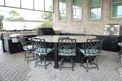 Photo of a large classic back patio in New Orleans with an outdoor kitchen, brick paving and a roof extension.