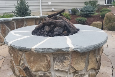 Example of a mountain style backyard concrete paver patio design in New York with a fire pit